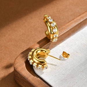 Gold-plated C-shaped hoop earrings with sparkling cubic zirconia on rustic linen display