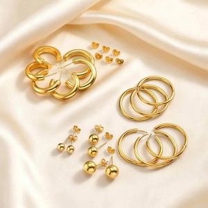 Detailed close-up of golden stainless steel hoop earrings and ball studs on silk