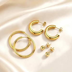 Detailed set of three golden stainless steel earrings on a soft cream satin background