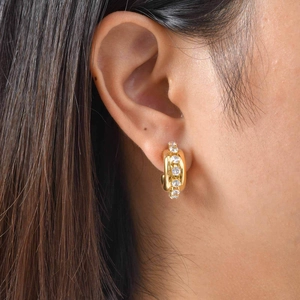Macro view of C-shaped golden earrings with inlaid round zircons on female model