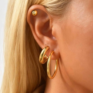 Close-up of model wearing gold stainless steel hoop earrings and ball stud set