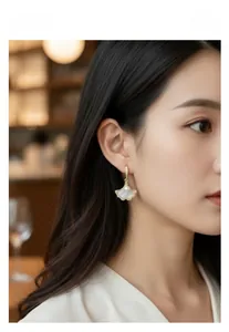 Gros plan de boucles d'oreilles feuille de ginkgo avec perle blanche et nacre sur modèle