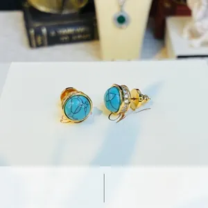 Macro shot of turquoise earrings with gold base and zircon circle on a white gift card