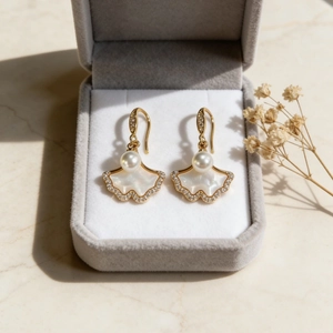 Boucles d'oreilles feuille de ginkgo dorées avec perles et cristaux sur un écrin