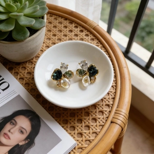 Detail of vintage flower earrings with crystal, green gems and pearls on a white tray