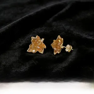 Macro shot of gold-plated caramel maple leaf earrings with crystals on black velvet