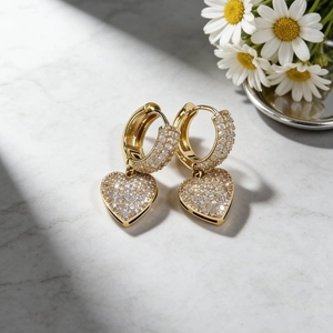 Orecchini a cuore dorati con micro-pave di cristalli su sfondo in marmo e fiori