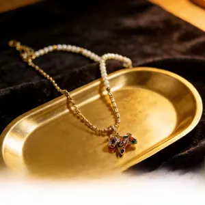 Macro detail of a pearl and gold chain necklace featuring a colorful zircon pony pendant