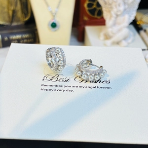 Macro shot of silver C-shaped pearl hoop earrings with zircon accents on a gift card