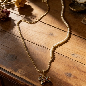 Charming pearl and gold chain necklace with a colorful enamel pony pendant on wood