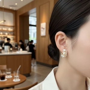 Flower cluster pearl earrings with a gold-tone finish shown on a female model