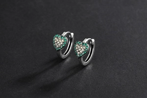 Détail de boucles d'oreilles en cœur avec pavé de zircons verts et blancs sur argent