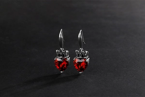 Close-up of gothic 925 silver earrings with heart red rubies and crown detailing