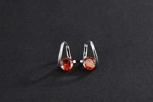 Detail of 925 sterling silver drop earrings featuring vibrant red round cut gemstones
