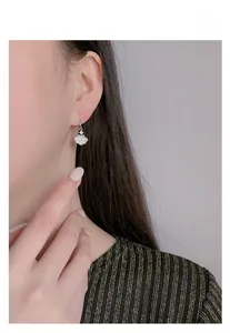 Detail of shell-shaped 925 silver drop earrings with mother of pearl on a model's ear