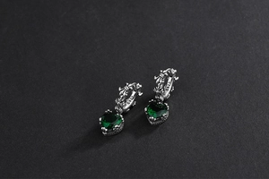Macro detail of S925 sterling silver heart earrings with green emerald and relief texture