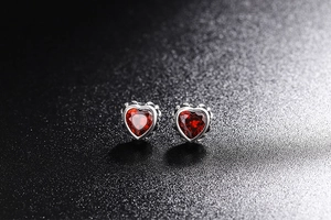 Macro detail of vintage 925 silver heart stud earrings with deep red gemstones
