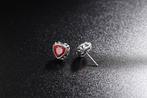 Macro shot of 925 silver heart earrings with ruby stones and gothic relief patterns