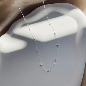 Gros plan d'un collier en argent s925 avec perles sur un support d'exposition blanc
