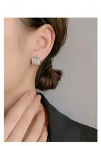Close-up of square silver earring with vintage cloud engravings on a female model