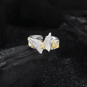S925 silver butterfly ring with gold rose relief on dark volcanic rock background