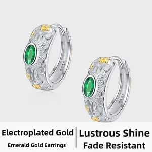 Macro detail of S925 sterling silver hoop earrings with gold floral relief and emerald zircon