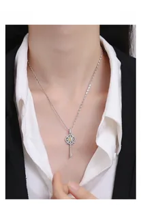Detailed view of silver key pendant with yellow gemstone on a white shirt and black blazer