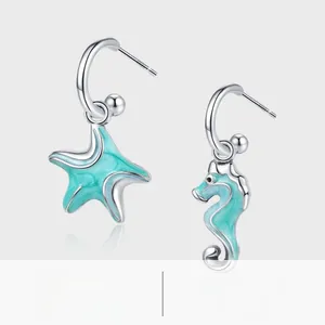 Macro detail of S925 silver hoop earrings featuring blue enamel seahorse and starfish