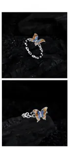 Détail macro d'une bague papillon émaillée avec dégradé orange et bleu sur anneau chaîne