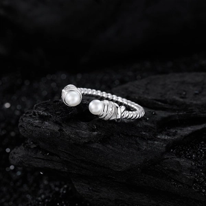 Bague torsadée en argent S925 avec deux perles et zircons sur support en pierre noire