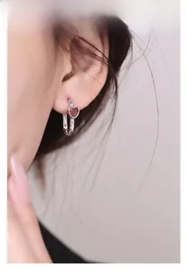 Macro view of S925 silver heart earring with red zircon stones worn on ear