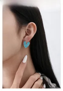 Close-up of a blue enamel heart earring with silver edges worn by a model for daily style
