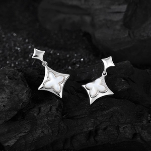 Silver S925 four leaf clover drop earrings with white shell on a black rock background
