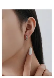 Close-up of S925 silver hoop earrings featuring small green heart-shaped zircons