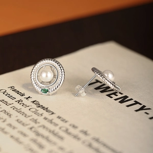 Vintage S925 silver pearl stud earrings with green gemstones on an open book