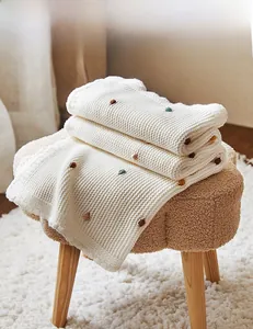 Close-up of cream cotton knit throw blanket featuring colorful textured popcorn stitch balls