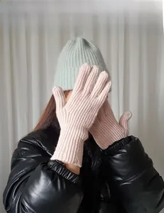 Détail de gants longs en maille côtelée rose portés avec un bonnet vert d'hiver