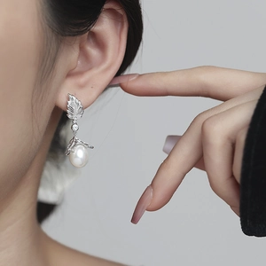 Detailed close-up of a silver leaf earring with a teardrop pearl on a model