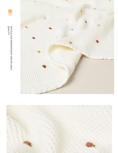 Close-up detail of white cotton knit blanket with colorful pom poms and mesh texture