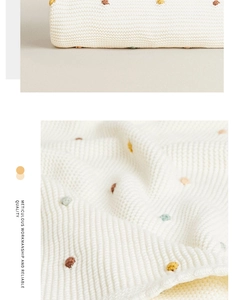 Detail of white knit blanket featuring colorful polka dots and meticulous workmanship
