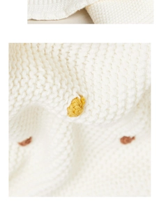Detailed close-up of white knitted cotton blanket with yellow and brown textured dots