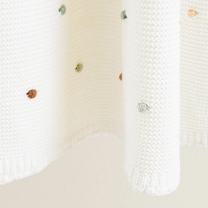 Minimalist white cotton knit blanket with colorful polka dots for cozy sofa lounging