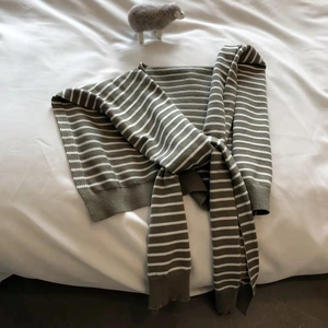 Knitted striped shawl wrap in olive green and white, laid flat with soft ribbing detail
