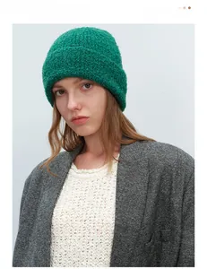 Detailed texture of thick dark green curly wool knit beanie on model for winter warmth