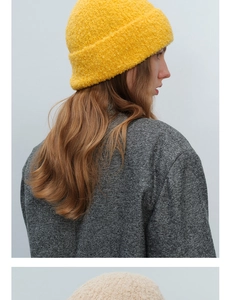 Detailed texture of yellow bouclé knit beanie paired with a herringbone wool coat