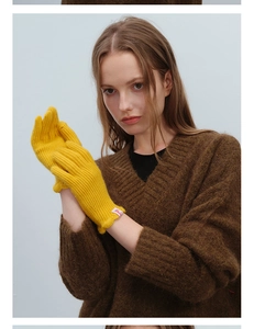 Detailed close-up of yellow knit wool gloves featuring red label and warm ribbed cuffs