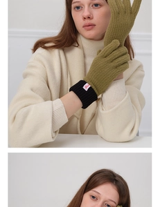 Close-up of olive green wool knit gloves with black ribbed cuffs and pink label detail