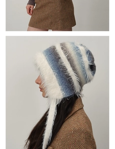 Detail of blue and gray striped knit beanie with white faux fur trim and long earflaps