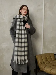 Close-up of classic black and grey plaid wool scarf with long tassel details on a model