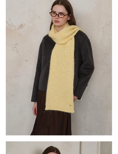Detailed texture of a pale yellow knitted scarf featuring a round metal button accent